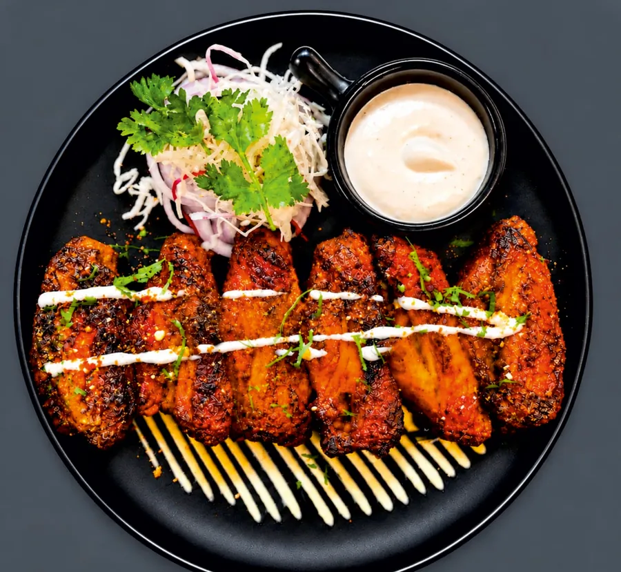 Nizami chicken wings on a black plate with salad and dip